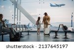 Airport Terminal: Beautiful Mother and Cute Little Daughter Wait for their Vacation Flight, Looking out of Window for Arriving and Departing Airplanes. Young Family in Boarding Lounge of Airline Hub