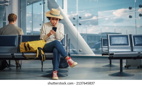 Airport Terminal: Black Woman Waits for Flight, Uses Smartphone, Receives Shockingly Bad News, Misses Flight. Upset, Sad, and Dissappointed Person Sitting in a Boarding Lounge of Airline Hub. - Powered by Shutterstock
