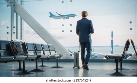 Airport Terminal: Businessman with Rolling Suitcase Walks, Uses Smartphone App for Internet e-Business. Traveling Entrepreneur Work Online while Waiting for a Flight in Boarding Lounge of Airline Hub