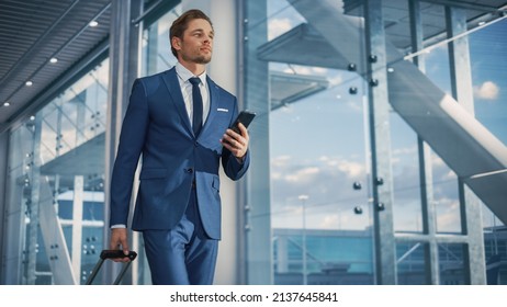 Airport Terminal: Businessman Walks to His Flight Gates, Uses Smartphone, Doing e-Business, Browsing the Internet with App. Digital Entrepreneur Remote Work Online While Traveling Through Airline Hub - Powered by Shutterstock