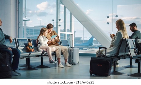 Airport Terminal: Cute Mother and Little Daughter Wait for their Vacation Flight, Play Educational Games on Digital Tablet. Young Family Sitting in Boarding Lounge of Airline Hub with Airplanes Flying - Powered by Shutterstock