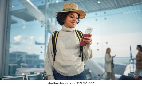 Airport Terminal: Happy Traveling Black Woman Looks Around Searching Flight Gates and Plane, Uses Smartphone, Checking Trip Destination on Internet. African American Female Wondering on Vacation