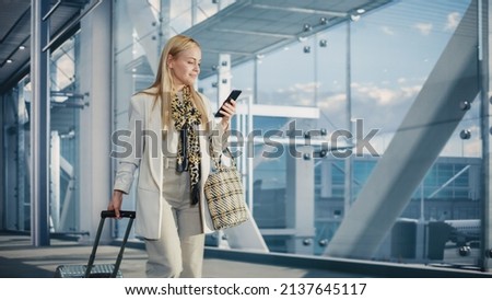 Airport Terminal: Happy Traveling Woman Walks to Her Flight Gates, Uses Smartphone, Browsing the Internet with App, Checking Traveling Destination. Female Walking Through Hallway of Airline Hub