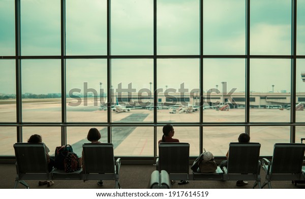 Airport terminal waiting seats for people family\
silhouette sitting resting waiting for plane to arrive with big\
window plane view of airport plane parking traffic, travel tourism\
transport concept