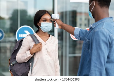 Airport Worker Checking Black Female Passenger's Temperature With Electronic Thermometer After Arrival, Covid-19 Outbreak Prevention