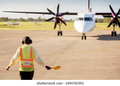 Airport Worker Signaling And Directing A Plane On The Airport Runway. Aviation Concept.