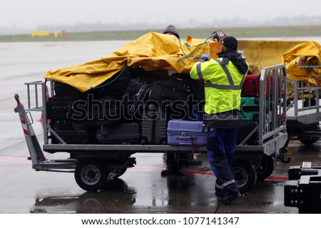 Airport workers cover passengers' luggage from the rain on a cart near the airplane.