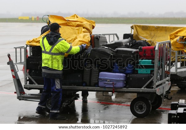 Airport workers cover passengers\' luggage from\
the rain on a cart near the\
airplane.