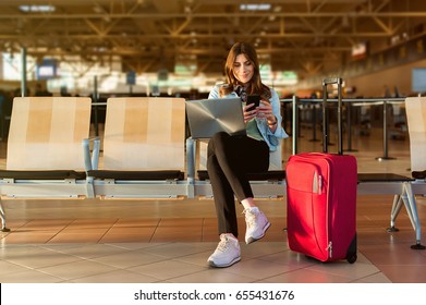 Airport Young female passenger on smart phone and laptop sitting in terminal hall while waiting for her flight