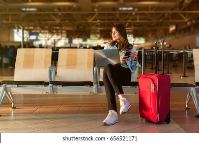 Airport Young Female Passenger On Smart Phone And Laptop Sitting In Terminal Hall While Waiting For Her Flight