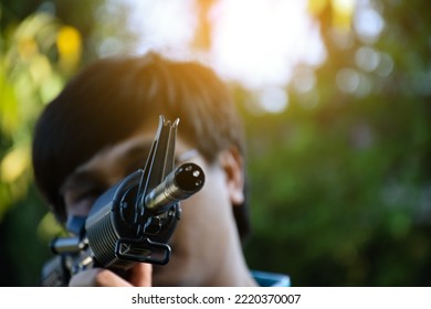 Airsoft Gun Or BB Gun Shooter Holds Airsoft Gun And Aiming It To The Shooting Target Point Ahead, Soft And Selective Focus On The Muzzle, Outdoor Recreational Activity Concept.