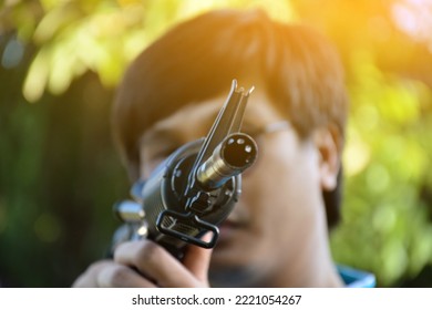 Airsoft Gun Or BB Gun Shooter Holds Airsoft Gun And Aiming It To The Shooting Target Point Ahead, Soft And Selective Focus On The Muzzle, Outdoor Recreational Activity Concept.