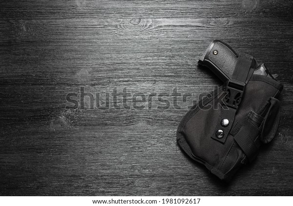 Airsoft gun in the holster on the black flat lay\
background with copy\
space.