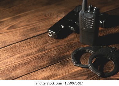 Airsoft Gun, Portable Radio Station And Bracelets On Brown Wooden Table Background With Copy Space. Detective Or Security Concept.