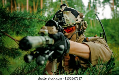 Airsoft man with optical sight gun. Soldier hidden into spruce branches on forest territory