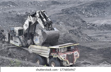 Ajmer, India - July 1, 2020 : Huge Dumper Earthmover Truck carrying minerals at an open pit quarry mines helped by a crane and other heavy machinery.