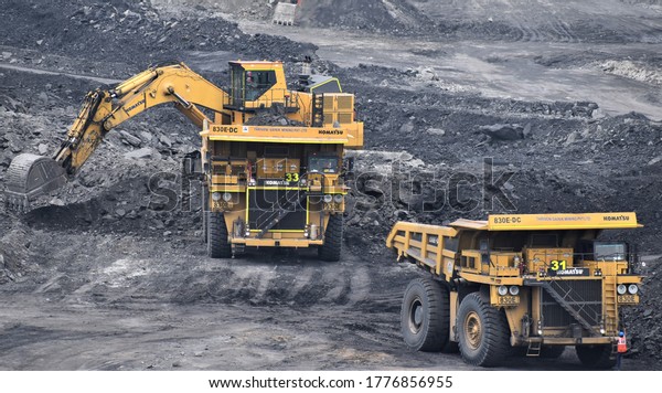 Ajmer, India - July 1, 2020 : Huge\
Dumper Earthmover Truck carrying minerals at an open pit quarry\
mines helped by a crane and other heavy\
machinery.