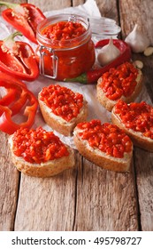 Ajvar in a glass jar and toast on a wooden background. Vertical, rustic