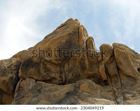 Alabama Hills boulders against blue sky with soft clouds, low angle looking up