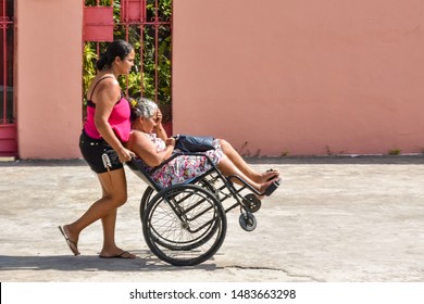 MACEIÓ, ALAGOAS / BRAZIL - AUGUST 19, 2019: Woman Pushing Wheelchair With Difficulty Due To Poor Conservation Of Sidewalks And Neglect Of Local Public Authorities.