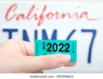 Alameda, CA - Apr 14, 2021:: Close up of hand holding California 2022 dated DMV tags with CA license plate in background.  Motor Vehicle registration must be renewed annually.