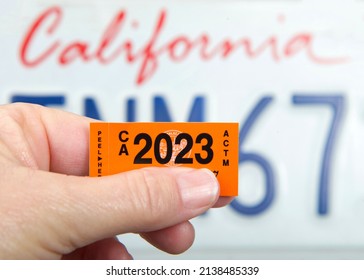 Alameda, CA - March 23, 2022: Close Up Of Hand Holding California 2023 Dated DMV Tags With CA License Plate In Background.  Motor Vehicle Registration Must Be Renewed Annually.