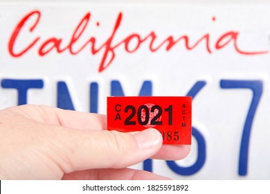 Alameda, CA - Oct 01, 2020: Close up of hand holding 2021 dated California DMV tags with CA license plate in background. Department of Motor Vehicle registration must be renewed annually.