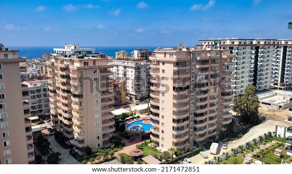 Alanya\
Antalya Turkey August 24, 2021. Several high-rise buildings on the\
coastline in Alanya. Ocean view and a clear blue sky in Alanya.\
Cars are parked on the road outside the\
building.