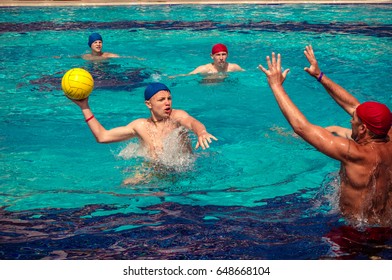 Alanya, Turkey - May, 3, 2017: A group of people playing in the pool in a water polo ball. Athletes in blue and red hats, yellow ball. These people tourists came to rest on vacation.