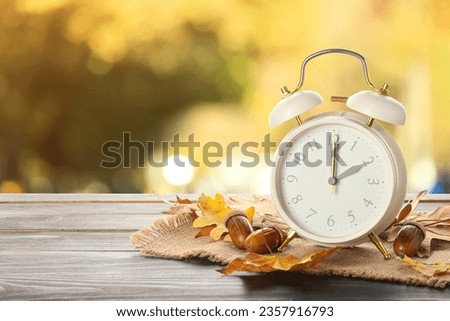 Alarm clock, acorns and autumn leaves on table outdoors. Daylight saving time end