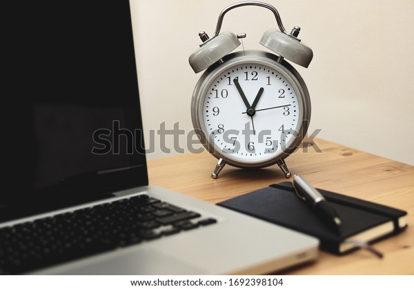 alarm clock alongside laptop and\
notebook in a workspace, time management concept, work from\
home