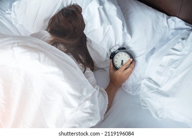 alarm clock and asian woman hand stop time in bed while sleeping, young adult female wake up late in the morning. Relaxing , sleepy, daily routine and have a nice day concepts