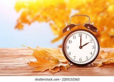 Alarm clock and autumn leaves on table outdoors. Daylight saving time end - Shutterstock ID 2205153363