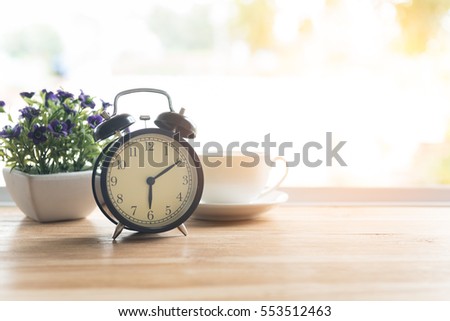 Alarm clock closeup have a good day with a cup of coffee and flower pots background in the morning sunlight.