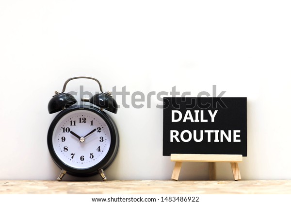Alarm clock and daily routine words blackboard on desk\
white background.   Chalkboard write routine text on table for copy\
space. 