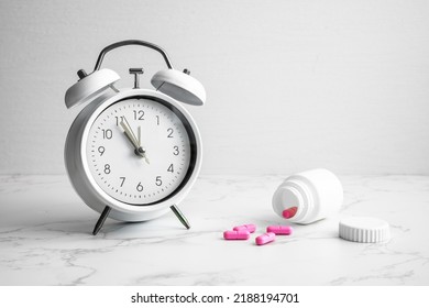 An Alarm Clock For Five To Twelve And Pink Pills On A Marbled Table. Medication, Reminder.