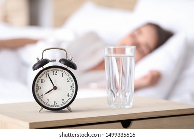 Alarm Clock And Glass Of Water On Table In Bedroom Of Young Woman