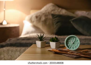 Alarm clock with magazines and houseplants on table in bedroom at night