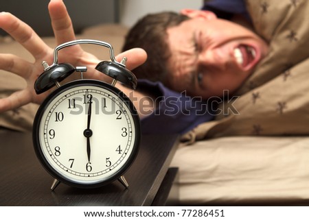 Alarm clock with male model in bed in background. Shallow depth of field.