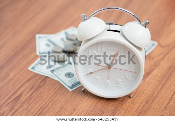 Alarm clock and money on\
wooden desk.