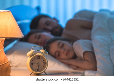 The Alarm Clock On The Background Of The Sleeping Family. Night Time