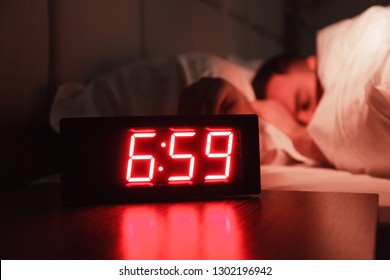 Alarm Clock On The Bedside Table With Red Numbers, Sleeping Man In Bed In Dark Room. Concept Chef Sleeping After Hard Day At Restaurant, Sleep Disturbance, Oversleep Work, Night Shift