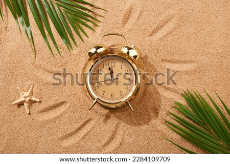 Alarm clock on a sandy beach. Noon, 12 p.m. A dangerous time for tanning and being in the sun.Sand texture, natural background. Top view.