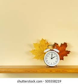 Alarm Clock On The Shelf With Maple Leaves. Autumn Time Change. Square.