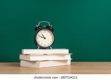 Alarm clock on stack of textbook with chalkboard on desk