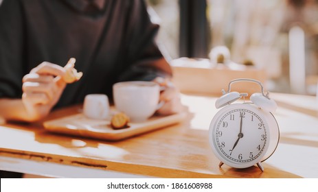 Alarm Clock On Wood Table With Blurred Woman Drinking Coffee. Morning Lifestyle Concept.