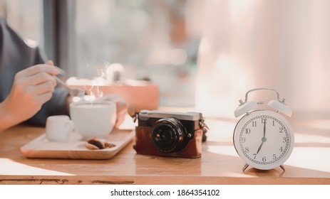 Alarm Clock On Wood Table With Blurred Woman Drinking Coffee. Morning Lifestyle Concept