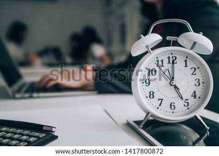 Alarm clock on wooden table with business discussion people group or meeting team background,Time concept at early morning or overtime in evening