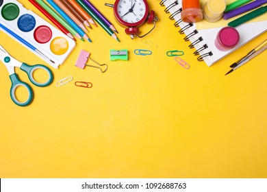 Alarm clock, paint, pencils and scissors. School accessories on a yellow background. View from above