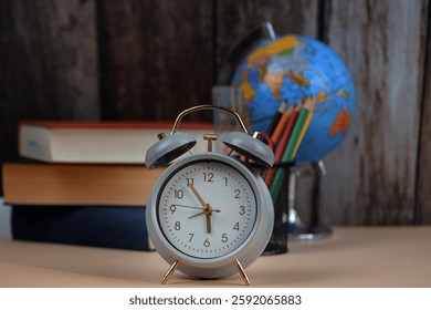 An alarm clock is placed on a table that is also adorned with several books and a globe, creating an interesting still life scene